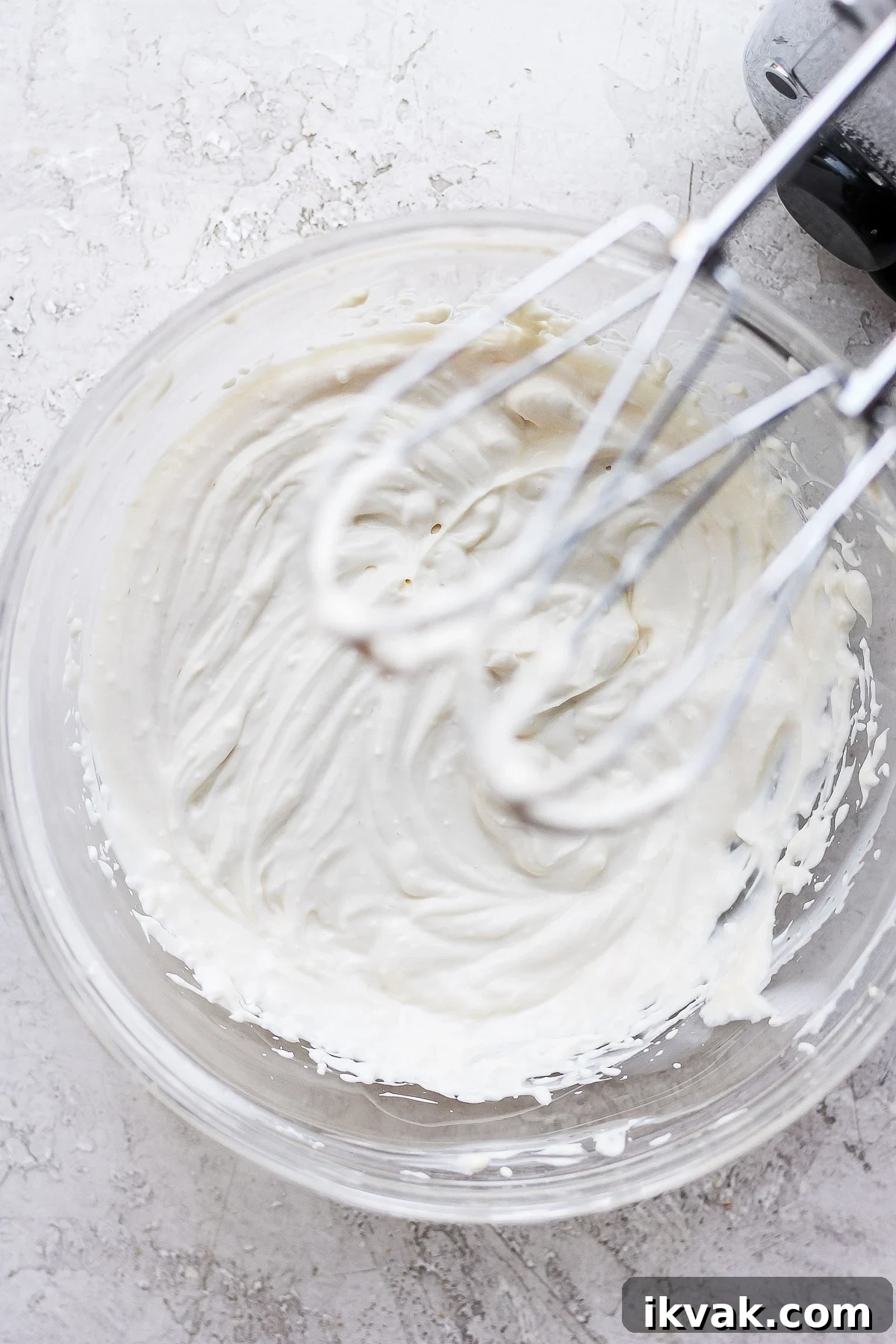 Cream cheese frosting with hand mixer in bowl.