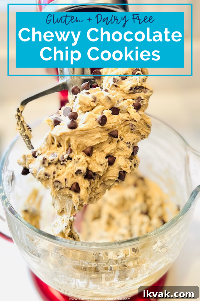 A stand electric mixer with the paddle attachment on and raw chocolate chip cookie dough all over it.