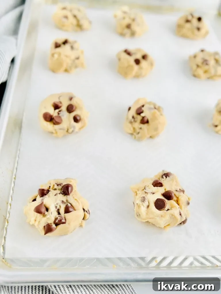 A large cookie baking sheet with raw cookie dough balls on it before it goes into the oven.