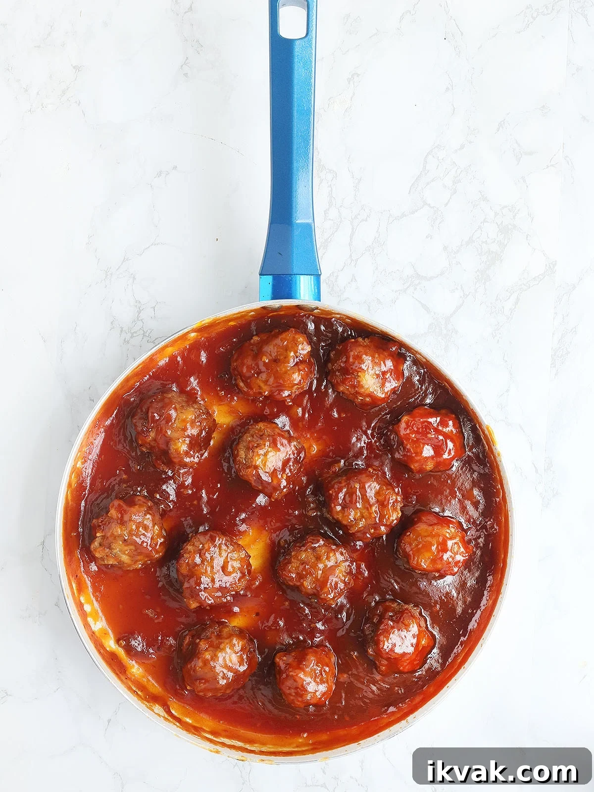 skillet of glazed meatballs on a white marble background