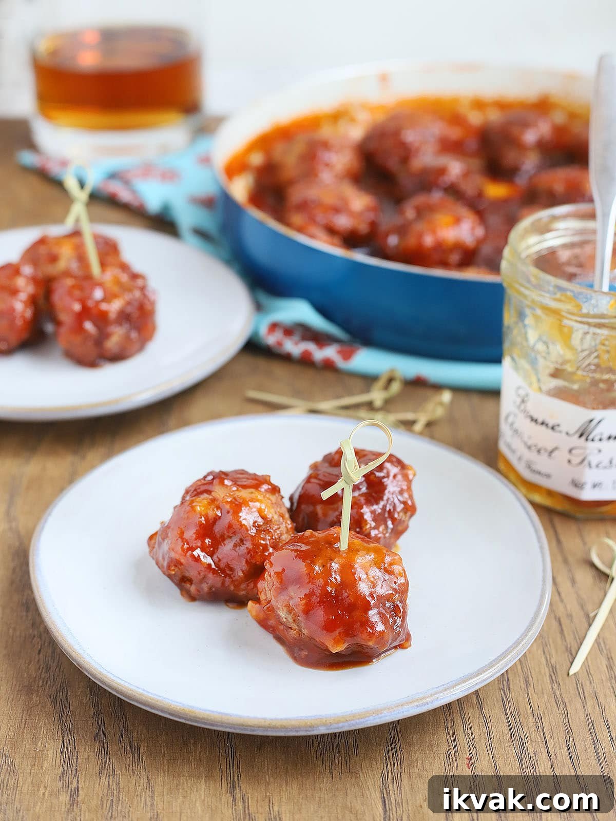 three glazed meatballs on a plate with a pan of meatballs in the background
