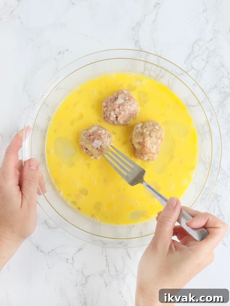hands coating three meatballs with egg