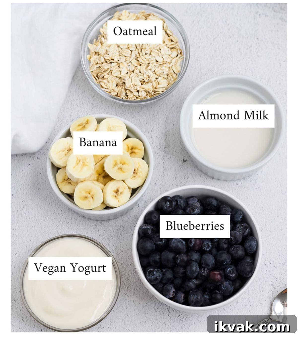 Blueberry Muffin Smoothie Recipe: Creamy Breakfast Shake 3 Picture of small clear and white bowls filled with oats, sliced bananas, blueberries, yogurt, and almond milk.