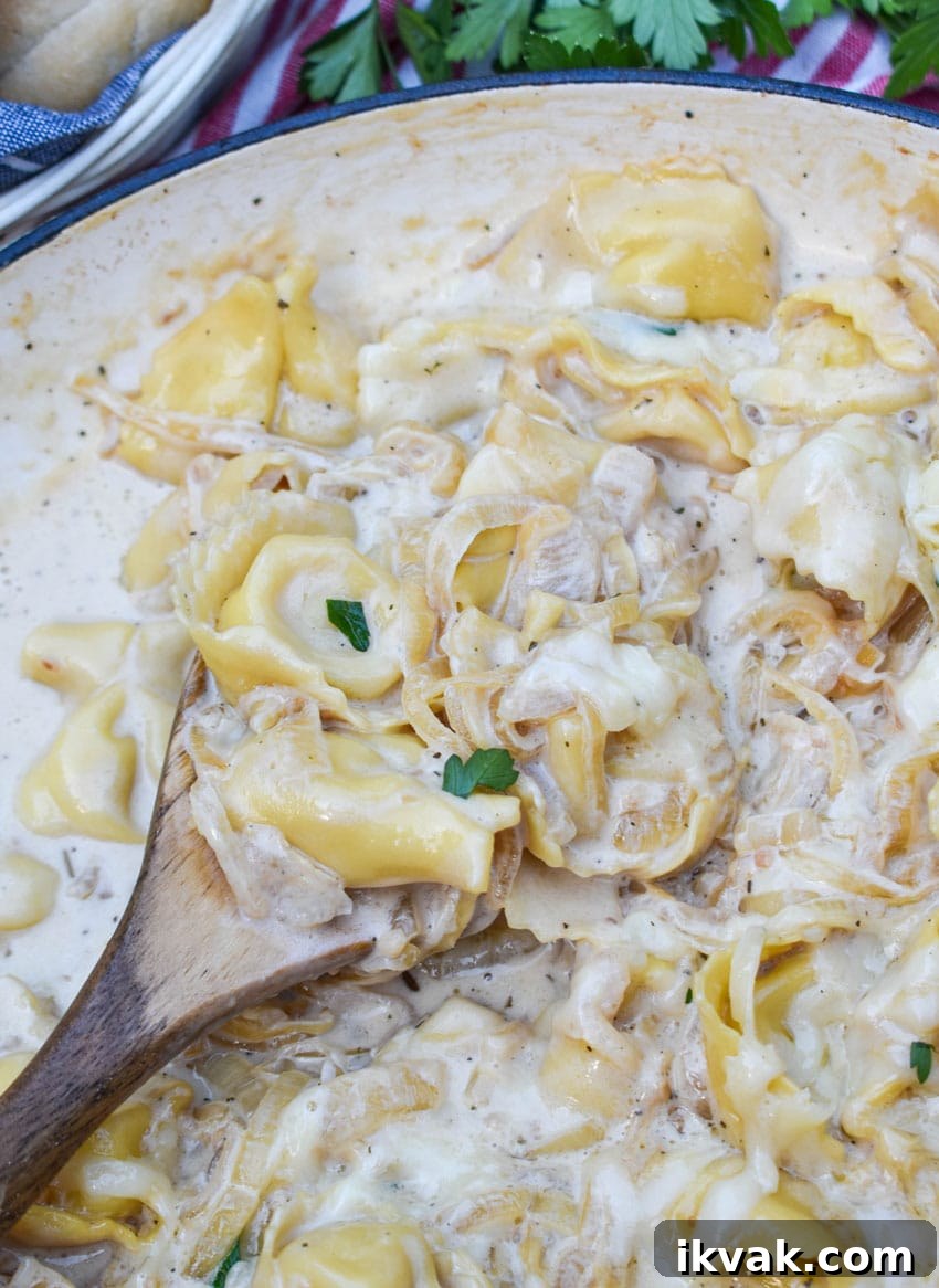 a wooden spoon scooping creamy french onion tortellini out of a cast iron skillet
