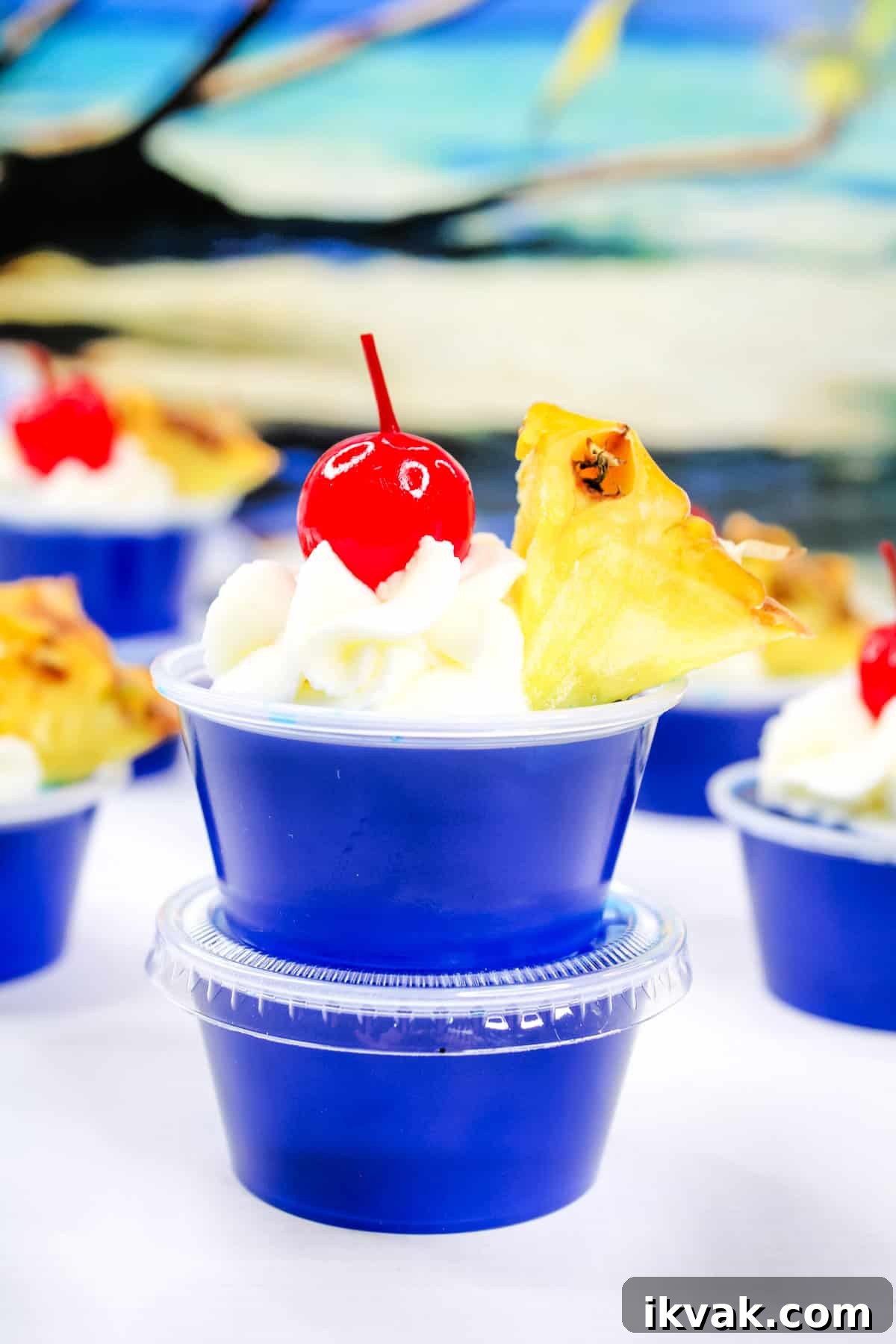 Malibu Coconut Rum Jello Shots Recipe for Summer Parties 2 blue raspberry Malibu Jello shots garnished with a pineapple wedge, whipped cream, and a marachino cherry.