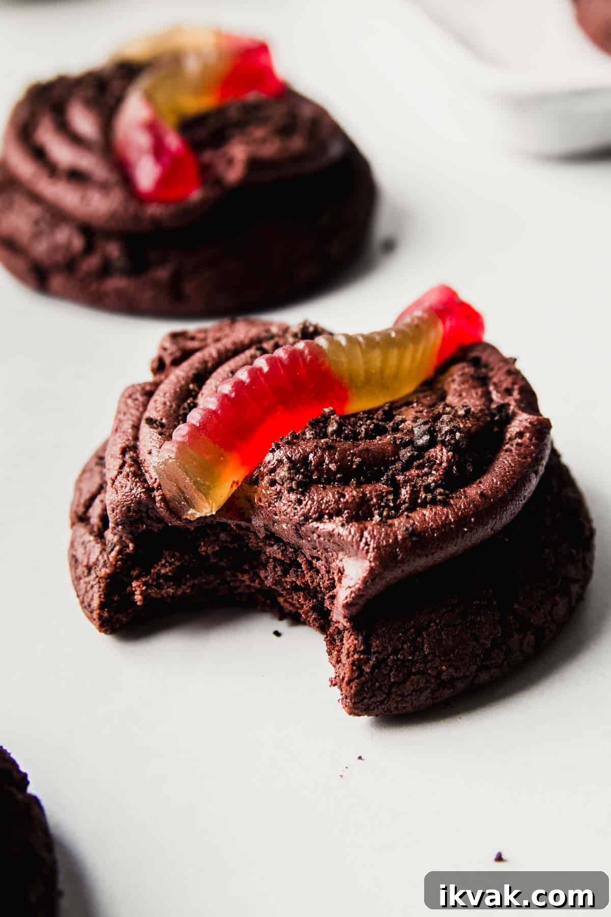 Chocolate cookie with buttercream icing, Oreo cookie crumbles, and gummy worm on top with bite taken.