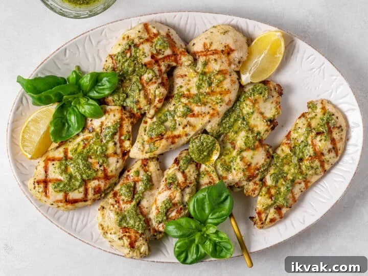 Grilled chicken with pesto, fresh basil, and lemon wedges on a white serving platter