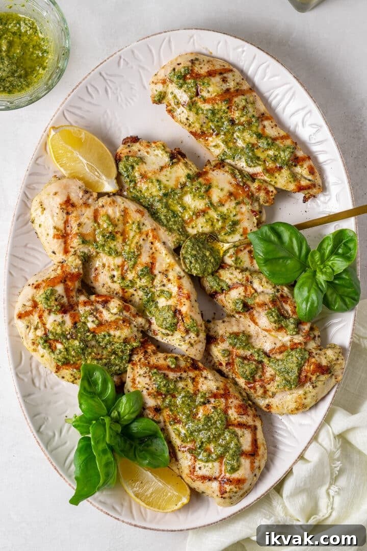 large white platter with grilled chicken dolloped with basil sauce, lemon wedges and fresh basil