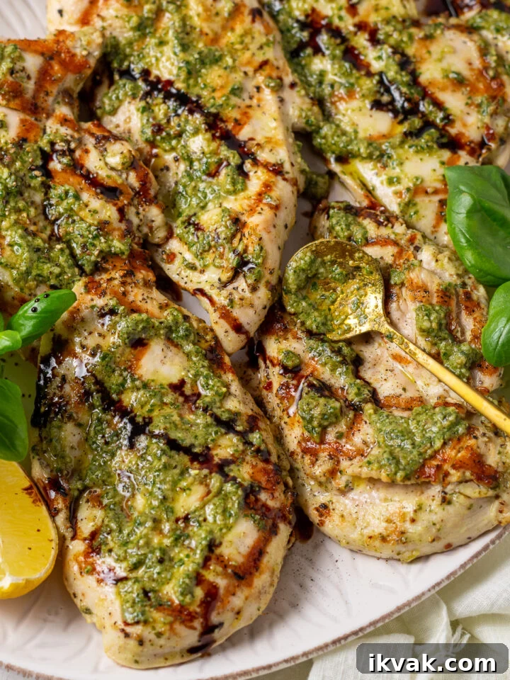 Close-up of grilled pesto chicken with basil pesto, balsamic glaze, lemon, and fresh basil