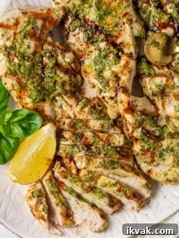 Sliced pesto chicken breast with basil pesto, balsamic glaze, fresh basil, and lemon on a serving platter.