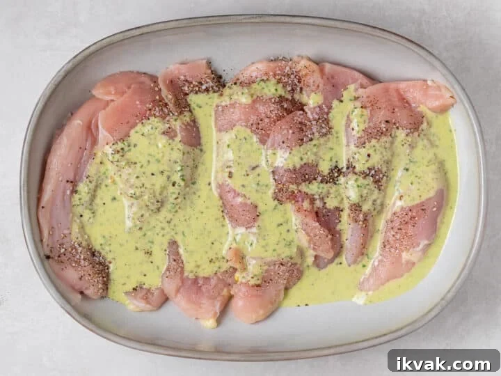 Raw chicken breast seasoned with salt and pepper and drizzled with pesto vinaigrette
