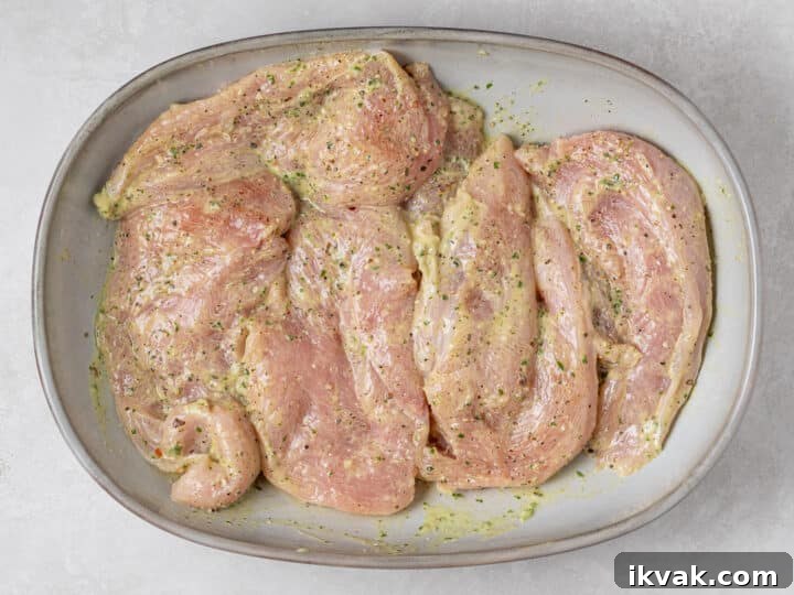 Raw chicken cutlets tossed with creamy pesto marinade in a shallow dish
