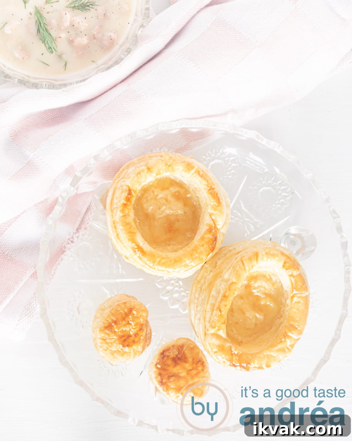 A photo from above of two homemade pie shells with lids on a glass plate. A pink checkered towel and a small part of a bowl filled with ragout above it