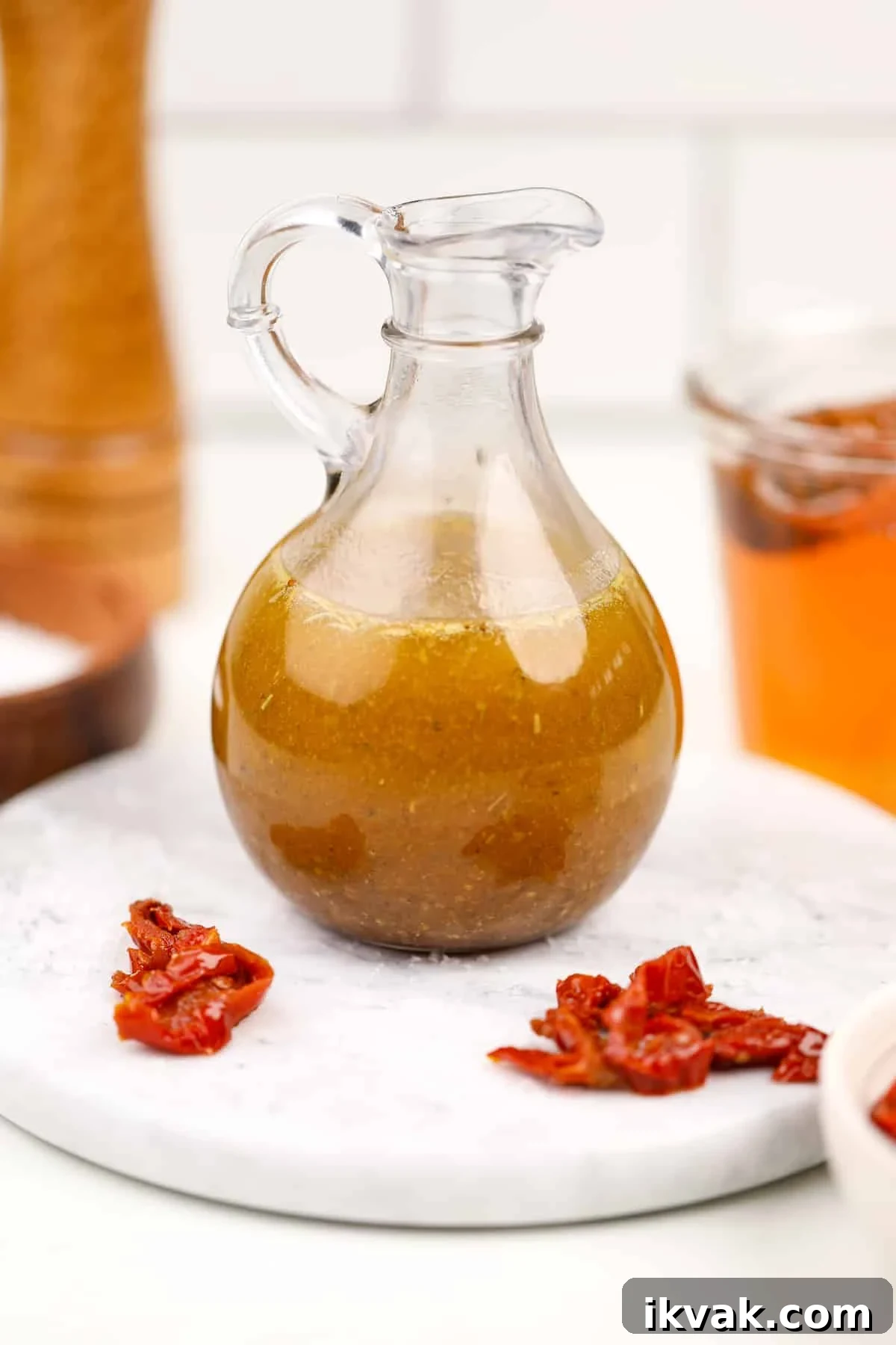 A cruet filled with homemade dressing; sundried tomatoes on the marble around it.