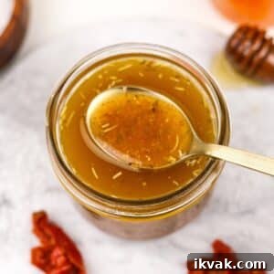 A small jar filled with homemade vinaigrette, a golden spoon taking a small amount.