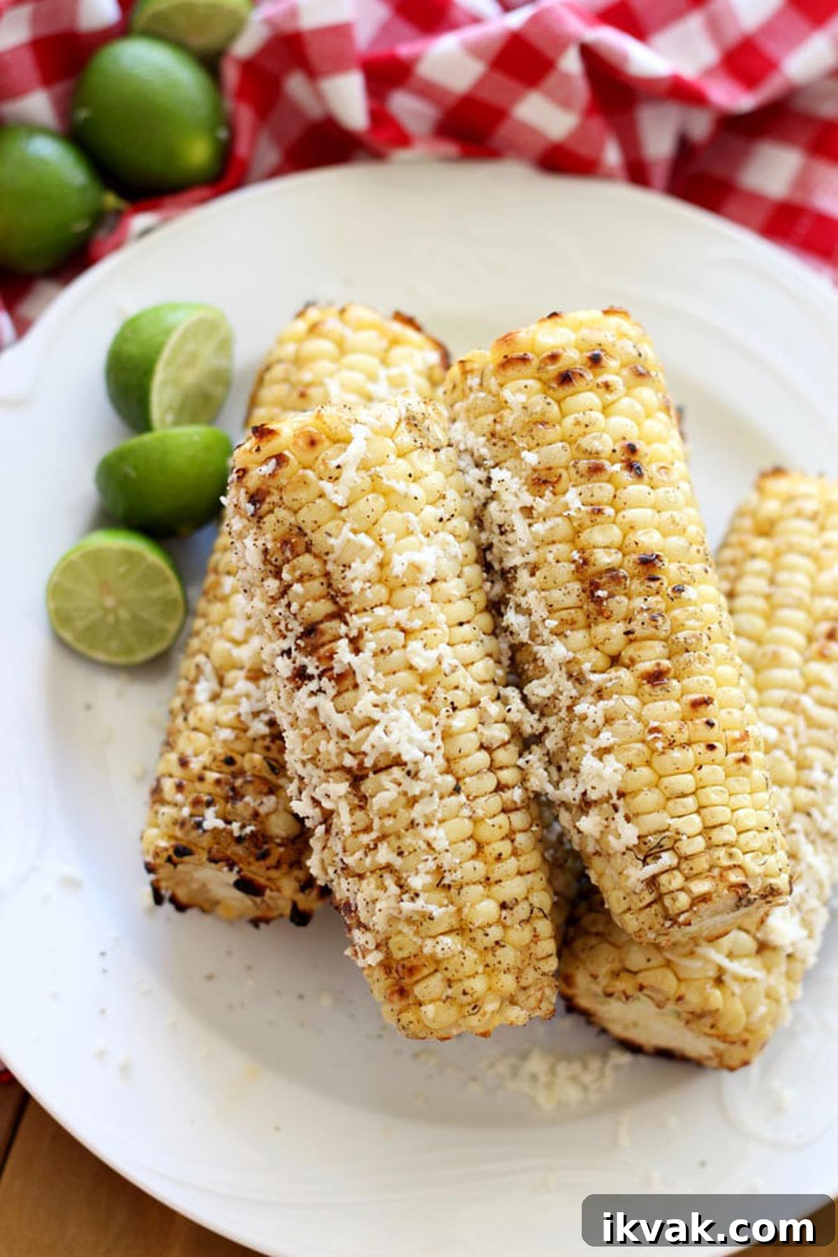 A close up of grilled corn on the cob covered with cotija cheese on a white plate.