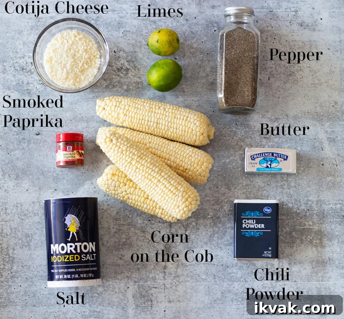 Cotija cheese, limes, pepper, salt, chili powder, paprika, corn on the cob, and butter on a counter.