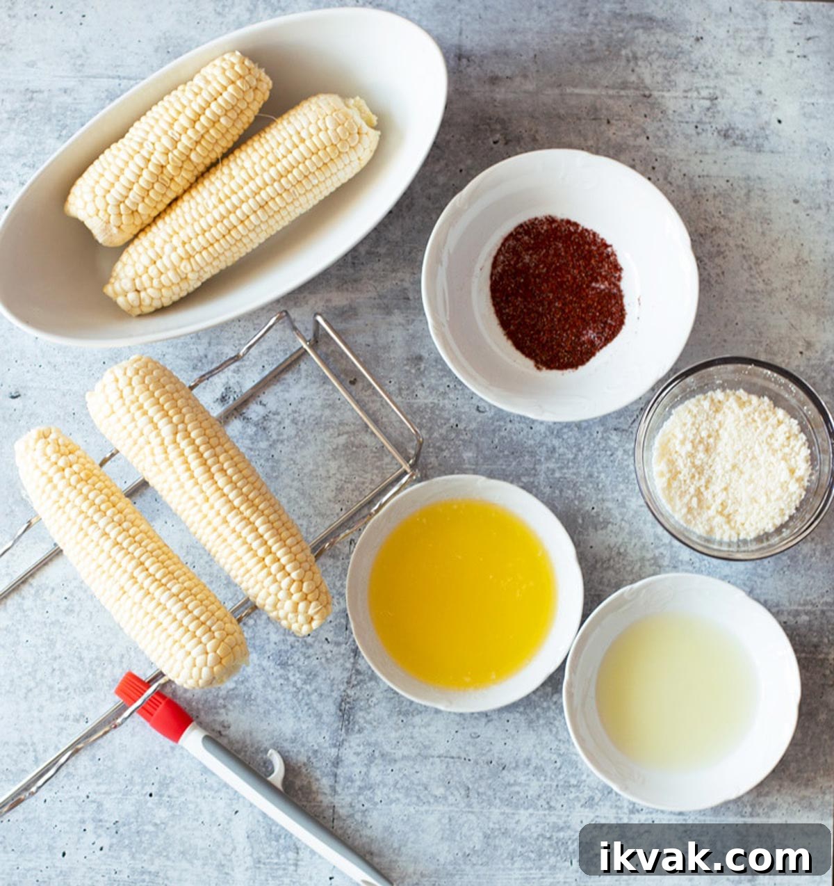 Corn on the cob on a table, bowls of butter, seasonings, lime juice, and cheese on table.