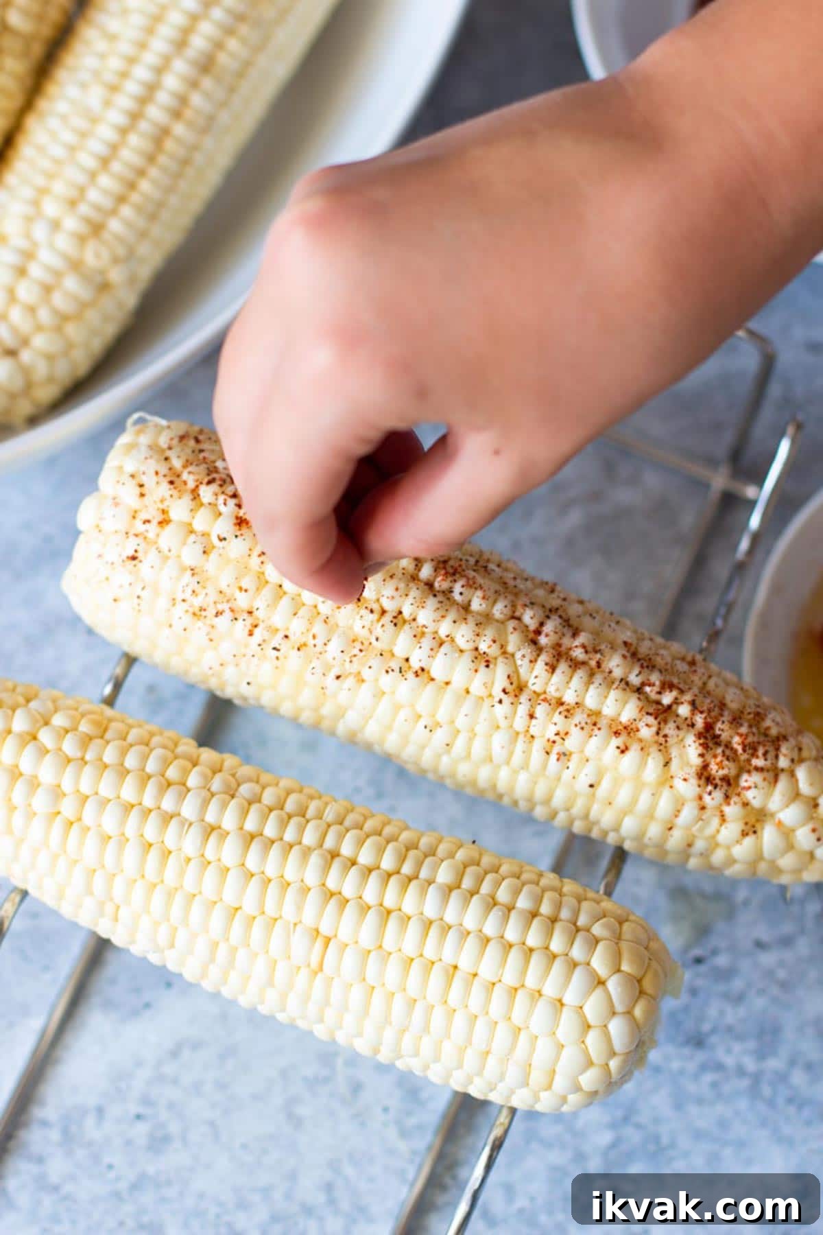 Person sprinkling on dry seasoning to make grilled Mexican corn on the cob.