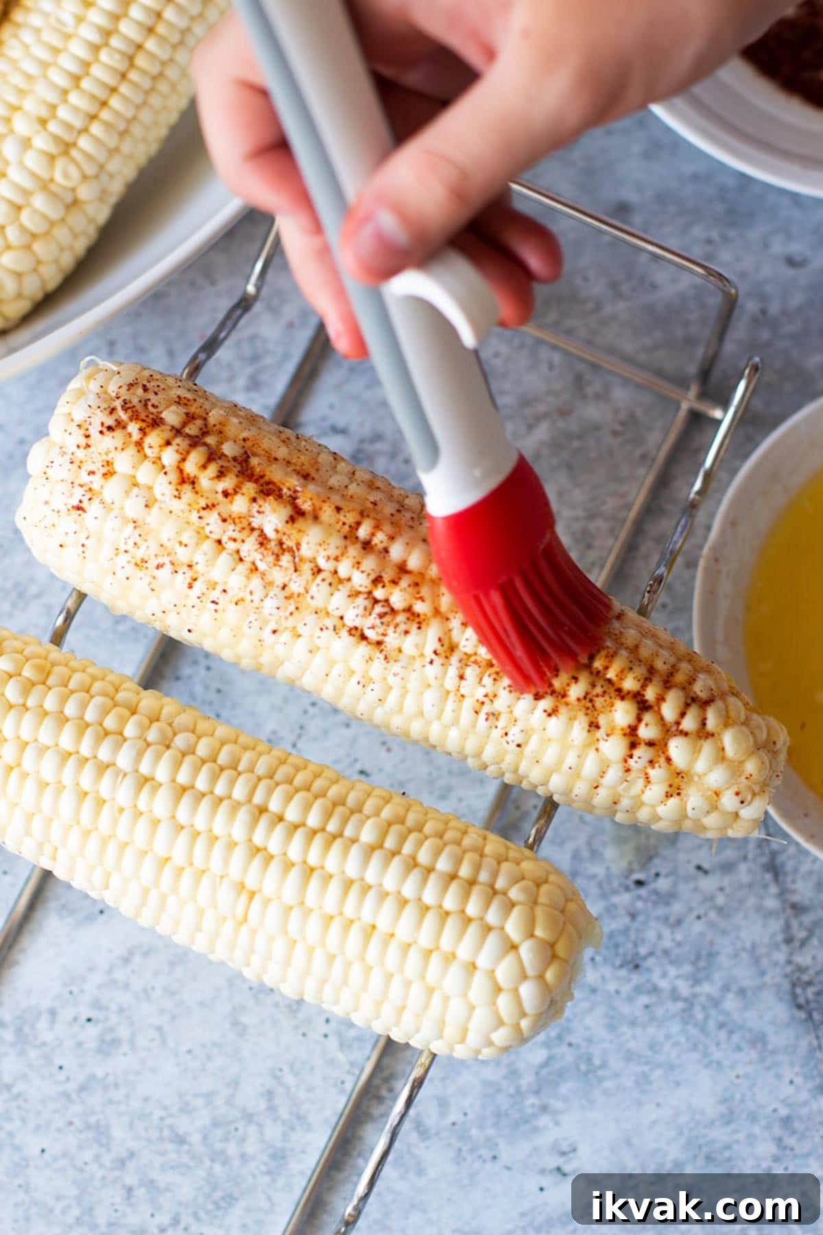 Person basting on butter to seasoned corn on the cob.