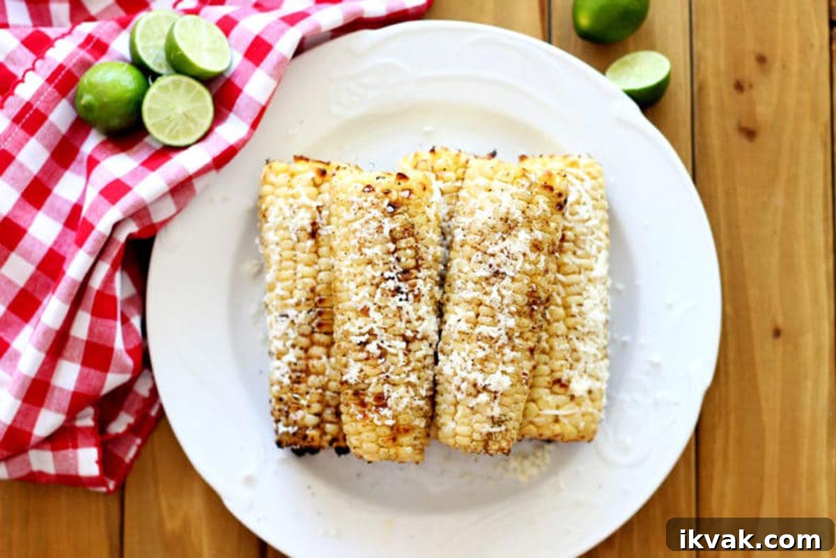 A white plate of five grilled corn on the cobs covered with cotija cheese.