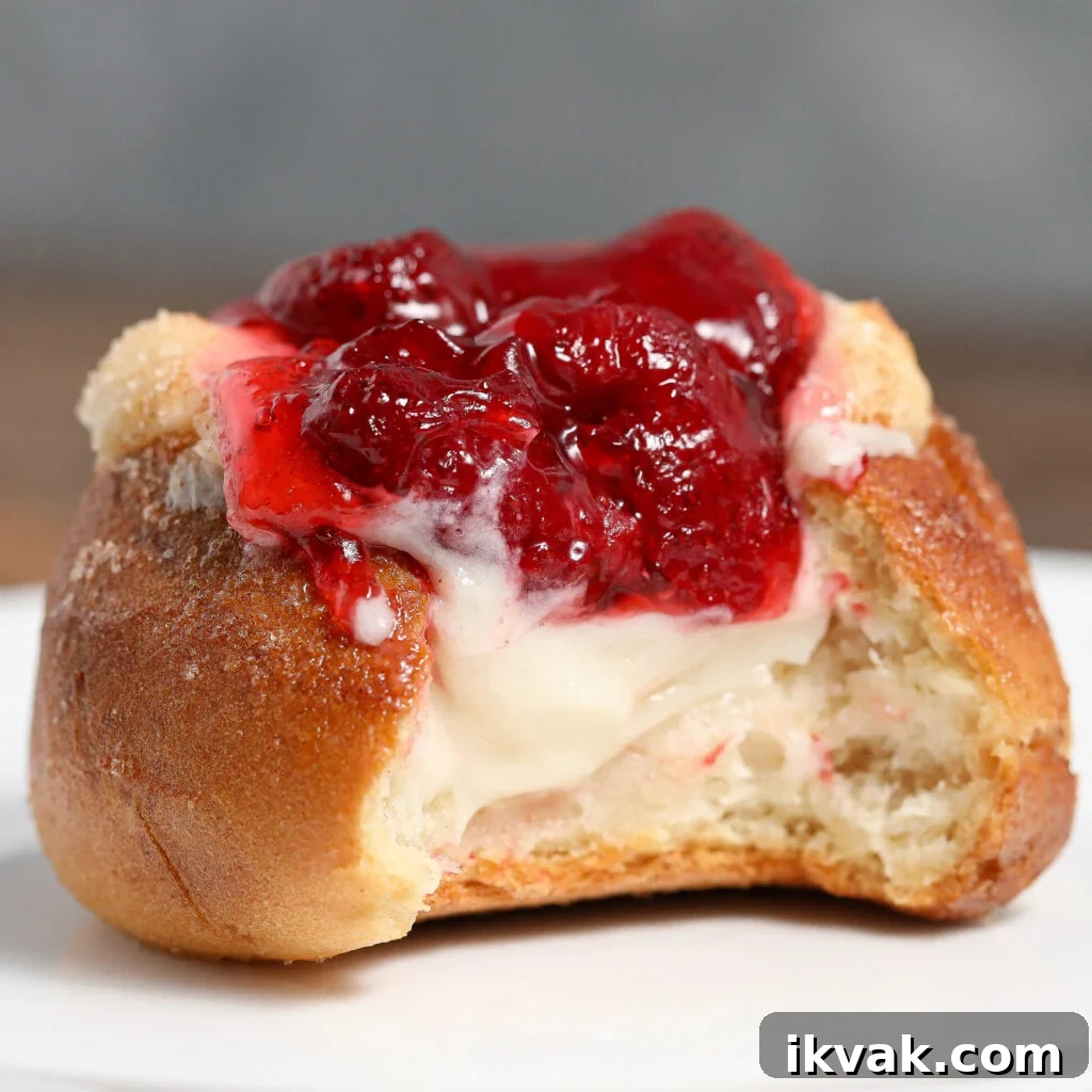 A partially eaten strawberry danish slider topped with glossy red strawberry filling and creamy white cheese, sitting on a white plate.