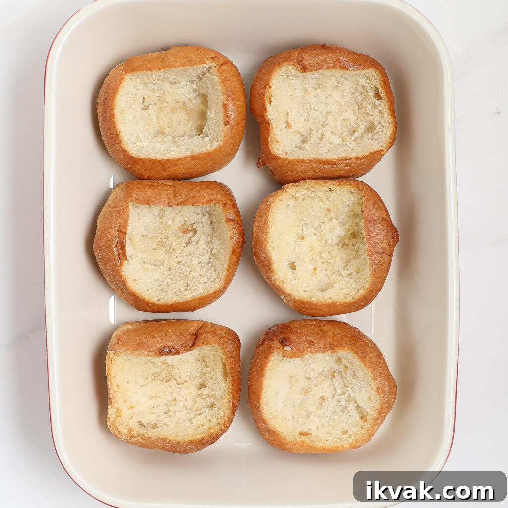 Six bread rolls with the centers hollowed out are arranged in two rows in a rectangular white baking dish, ready to be transformed into irresistible strawberry danish sliders.