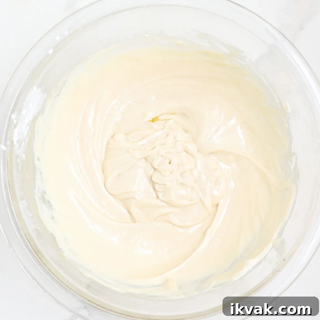 A glass mixing bowl filled with smooth, creamy, pale batter or frosting—perfect for strawberry danish sliders—swirled in the center and sitting on a white surface.