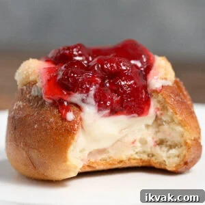 A partially eaten strawberry danish slider topped with glossy red strawberry filling and creamy white cheese, sitting on a white plate.