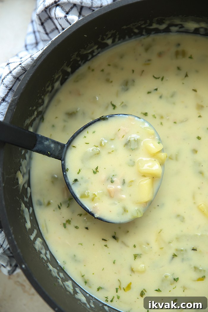 A large pot of Classic Clam Chowder with a soup ladle with chowder held above the chowder.