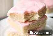 A white plate with a stack of three sugar cookie bars stacked on top of each other with a bite out of a corner of the top bar. Faded in the background are more cut frosted sugar cookie bars. Overlaid at the bottom is the text 