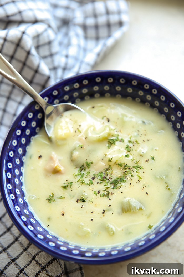 Classic clam chowder in polka dotted soup bowl with a spoon inserted at the top. A checkered patterned tea towel is wrapped around the left of the bowl.