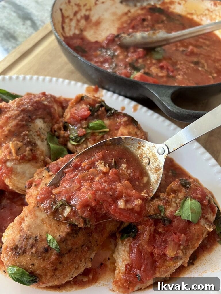 Spooning additional pan sauce over the plated chicken pomodoro in white serving platter.