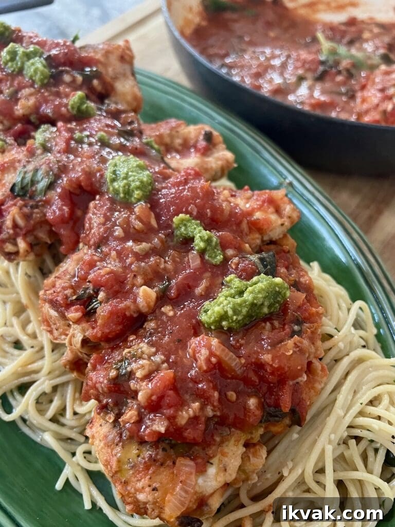 One Pan Chicken Pomodoro over a bed of spaghetti with garlic and olive oil, topped with a few spoonfuls of basil pesto.