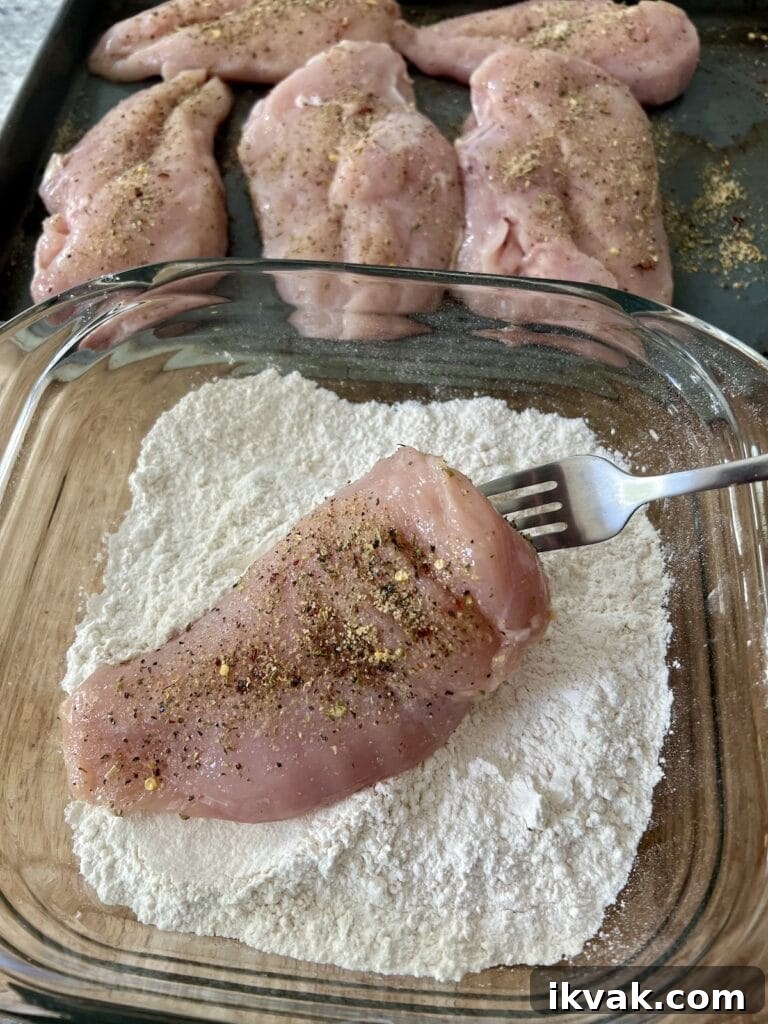 Coating one chicken breast in flour using fork.