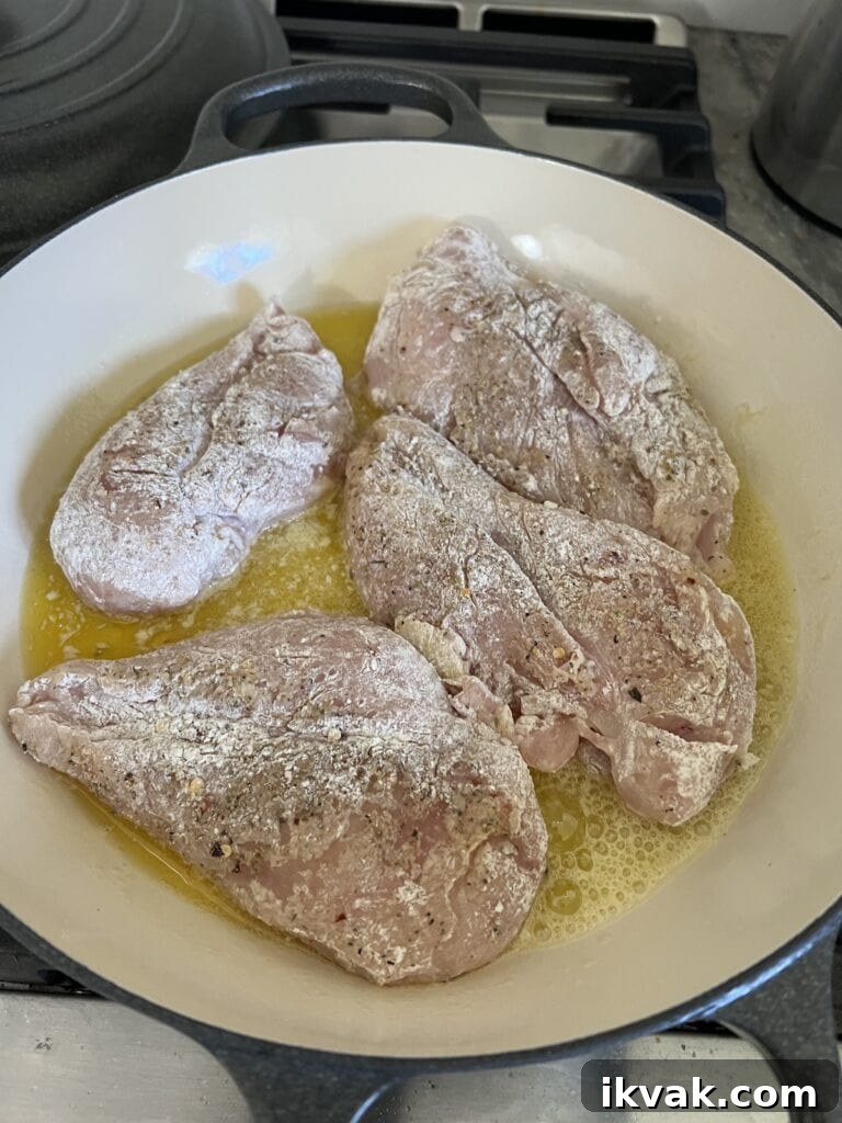 Searing the seasoned and floured boneless, skinless chicken breast in an oil and butter combination in pan.