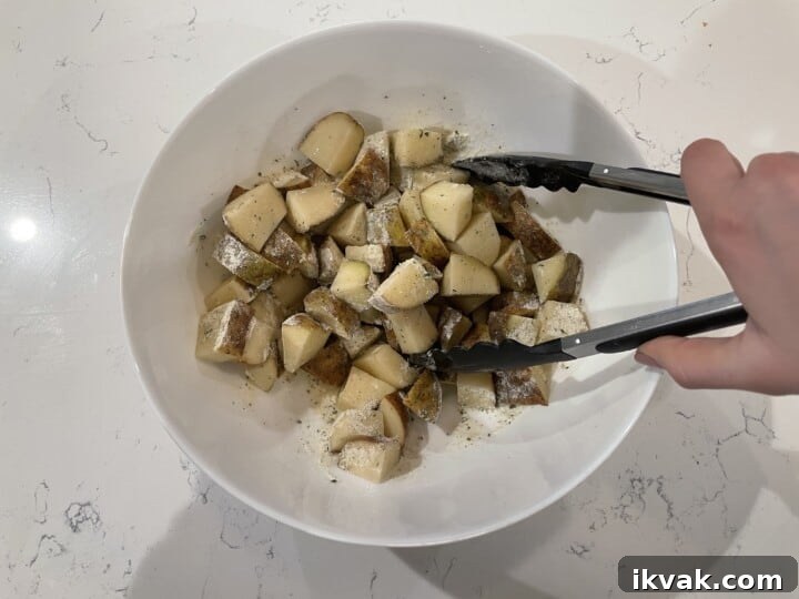 mixing potatoes oil and ranch seasoning in white bowl