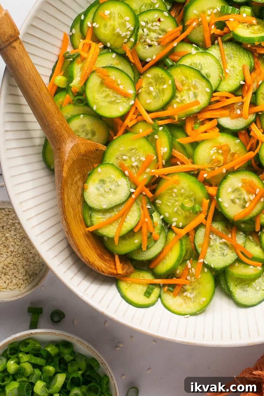 Crisp Cucumber and Carrot Salad with Tangy Dressing 2 a bowl filled with sliced cucumbers, carrots, and sesame seeds with a wooden spoon resting on the side