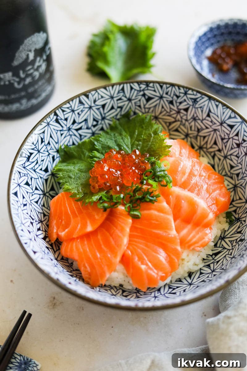 Salmon sashimi donburi with shiso, Ikura, and scallions in a blue and white bowl.