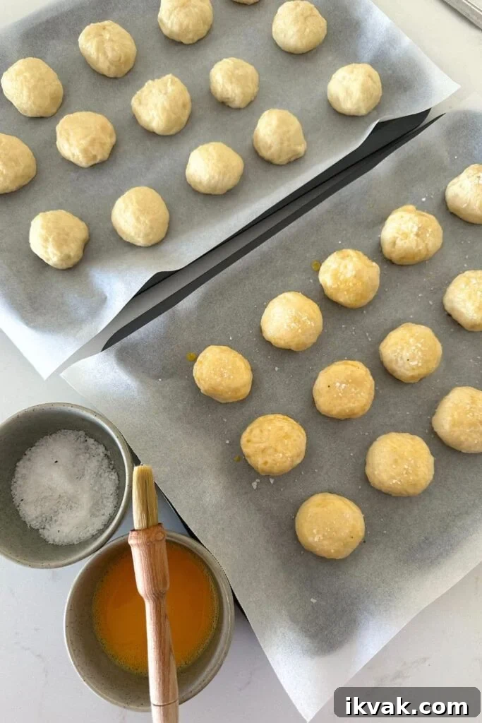 Sourdough discard pretzel bites that have been boiled and are sitting on a baking tray. They are being brushed with egg wash and sprinkled with coarse flaky sea salt.