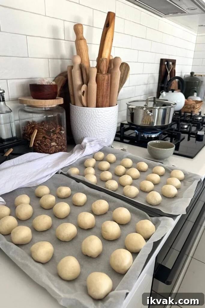 Sourdough discard pretzel bites sitting on a baking tray in a modern kitchen. You can see a pot of rolling pins in the background, as well as pot of water boiling on the stove top in preparation for boiling the sourdough discard pretzel bites.