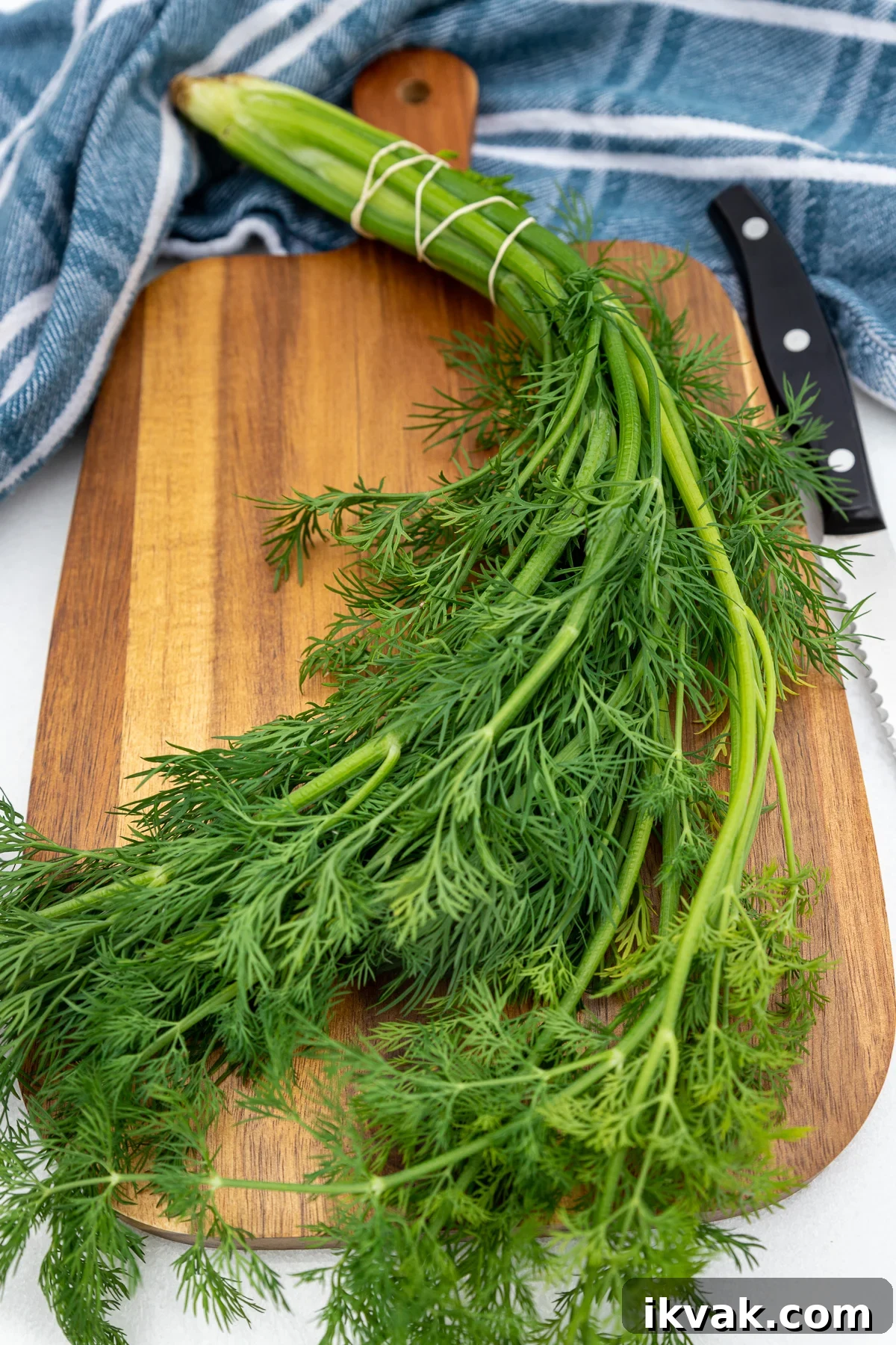20 Flavorful Dill Substitutes for Cooking and Garnish 2 A bunch of fresh green dill on a wooden chopping board with a knife and a blue and white tea towel behind.