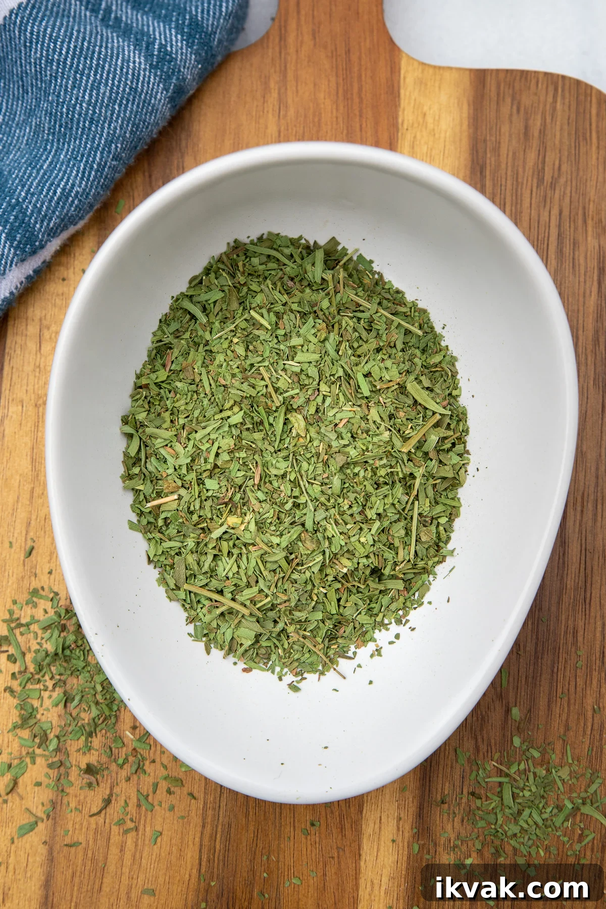 20 Flavorful Dill Substitutes for Cooking and Garnish 5 Dried tarragon in a white bowl on a wooden board next to a white and blue tea towel.