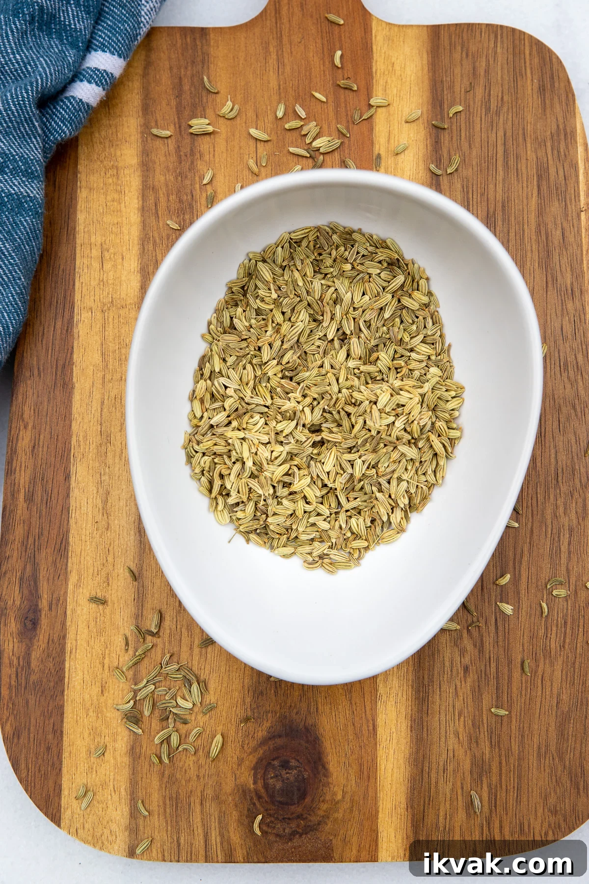 20 Flavorful Dill Substitutes for Cooking and Garnish 9 Dried fennel seeds in a small white bowl on a wooden chopping bowl and with the edge of a blue and white tea towel on the left.