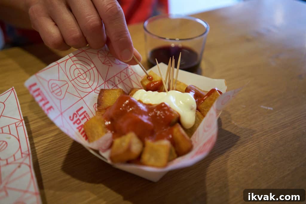 A woman's hand holding a toothpick used to eat Patatas Bravas - fried potatoes with tomato sauce and mayonnaise.