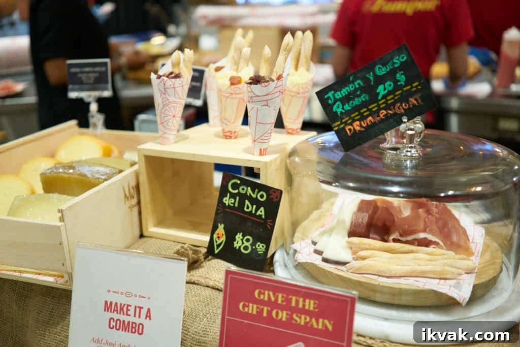Cones with cheese, charcuterie and breadsticks on display next to the same ingredients under a glass dome.