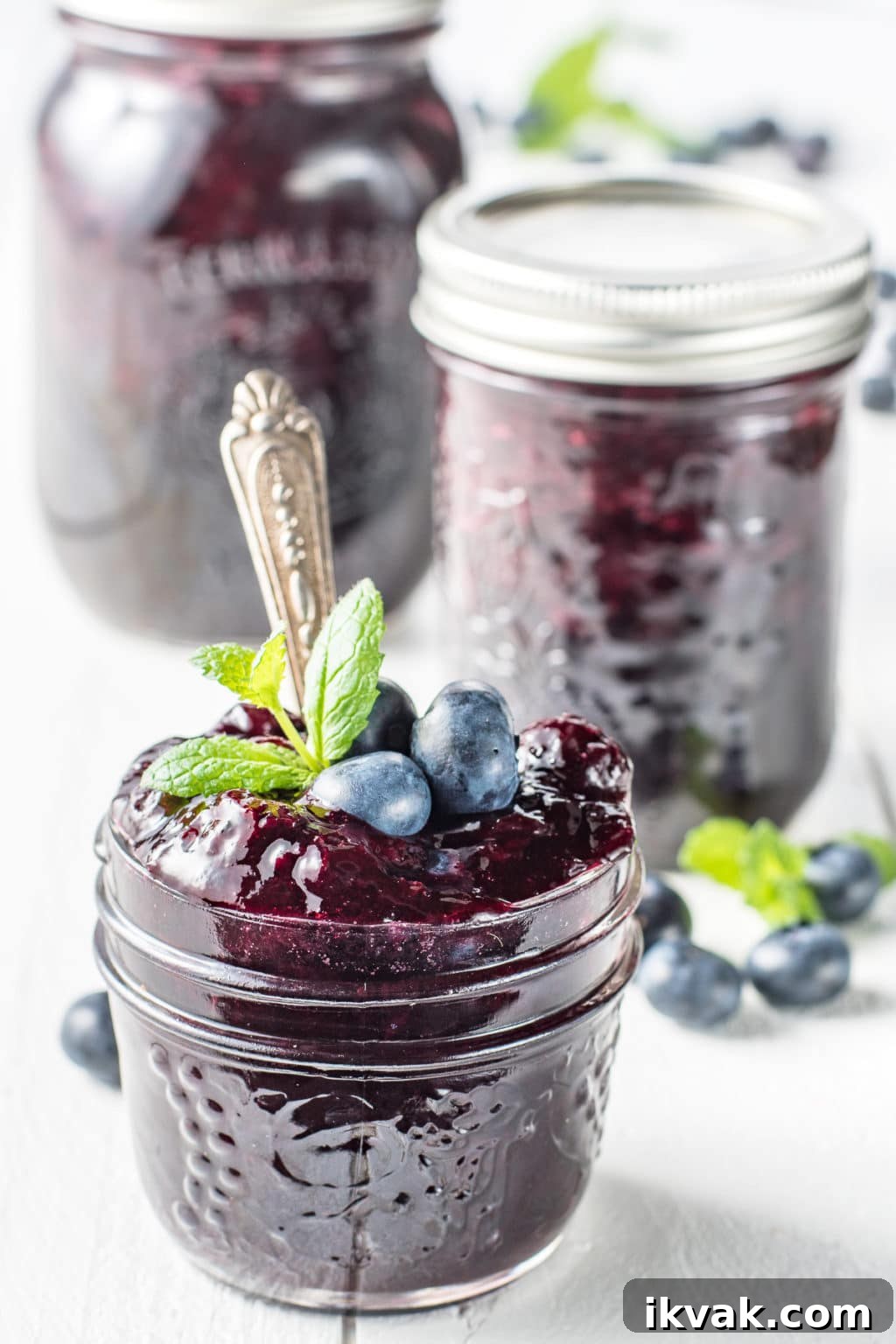 Jars of sugar-free blueberry jam on a white wooden board with sprigs of mint and scattered fresh blueberries