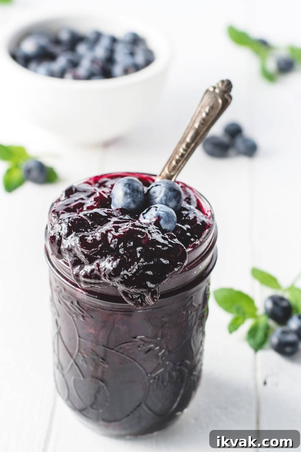 A jar of sugar-free blueberry jam with a large drip running down the side of the jar on a white background