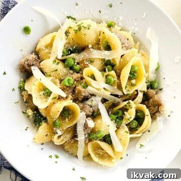 A bowl of shell pasta with green peas and Italian sausage.