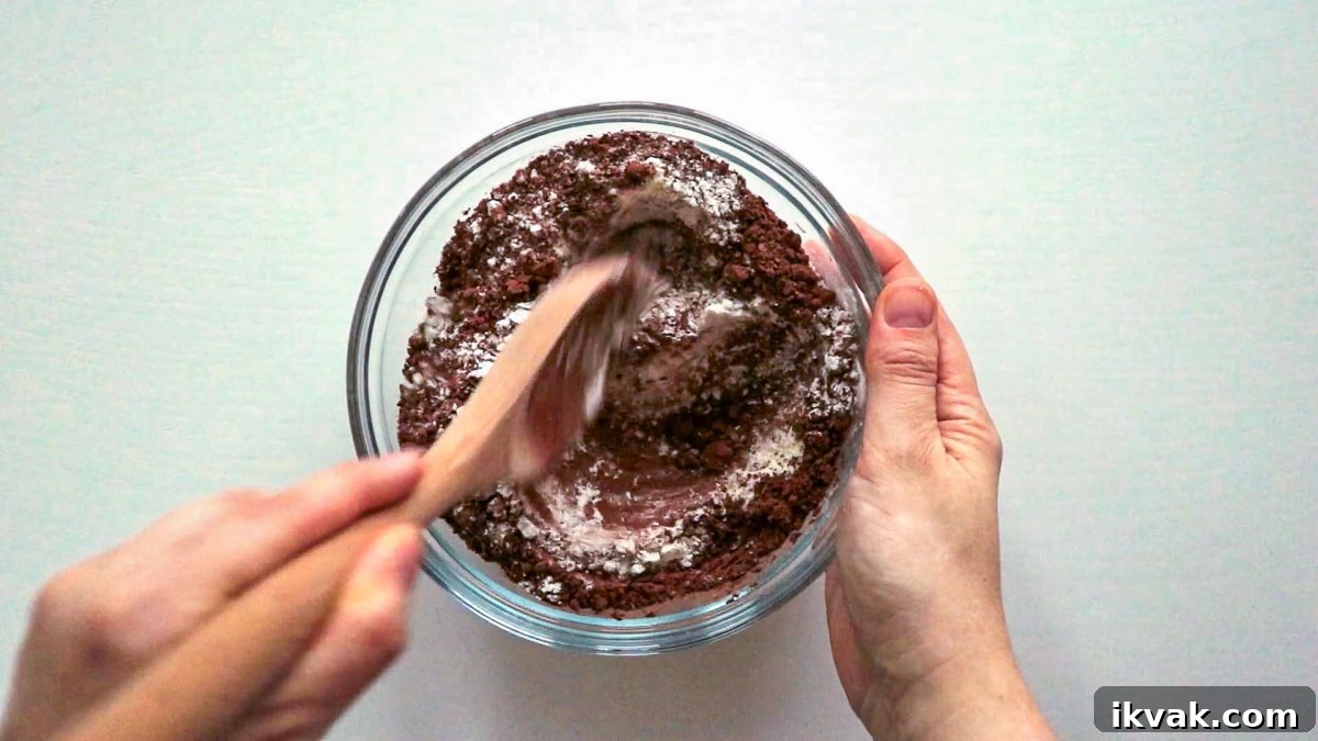 Dry ingredients in a glass bowl, hand using a wooden spoon to mix them.